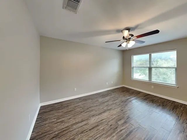 an empty room with wooden floor chandelier fan and windows