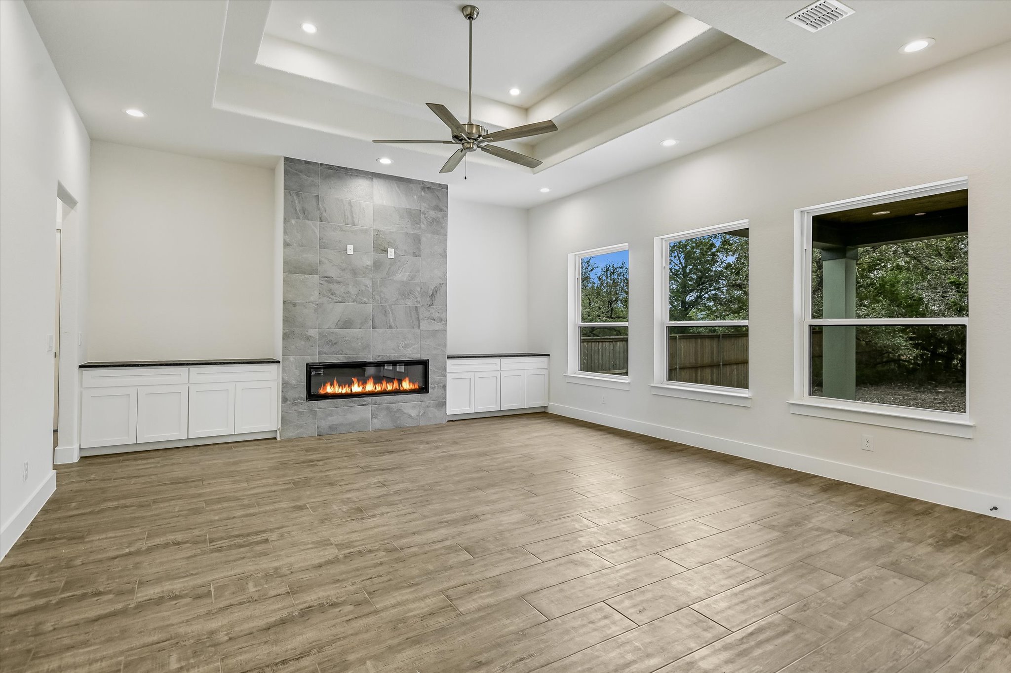 32 Peace Pipe Wimberley, TX 78676 - Photo 5 of 20 Unfurnished living room with ceiling fan, a tile fireplace, light wood-style floors, recessed lighting, and a raised ceiling