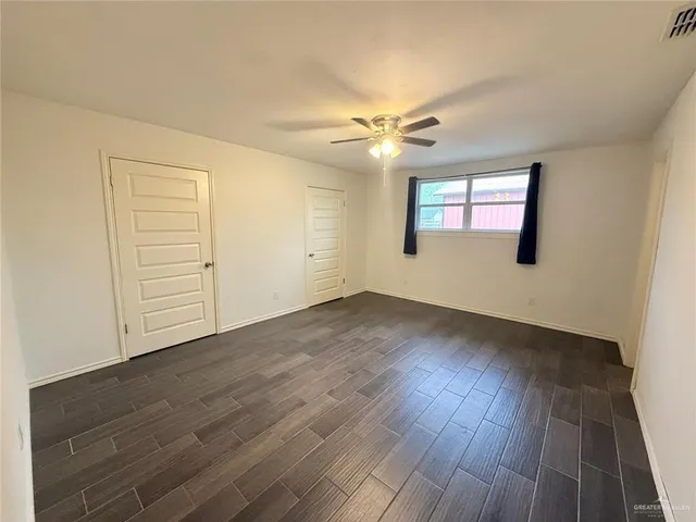 an empty room with wooden floor chandelier fan and windows