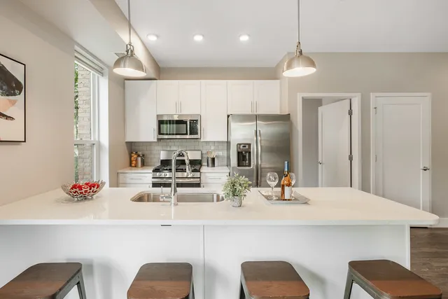 a kitchen with stainless steel appliances kitchen island granite countertop a dining table chairs refrigerator and sink