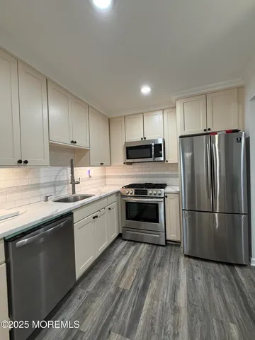 a kitchen with stainless steel appliances granite countertop a refrigerator a sink dishwasher a stove and white countertops with wooden floor