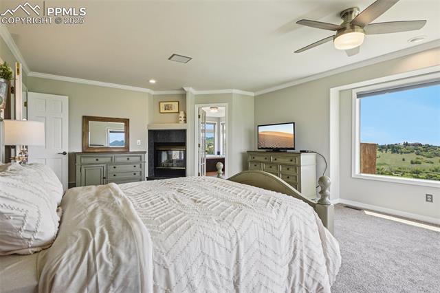 14425 Granby Road Colorado Springs, CO 80921 - Photo 31 of 45 Carpeted bedroom with multiple windows, ornamental molding, baseboards, a multi sided fireplace, and a ceiling fan