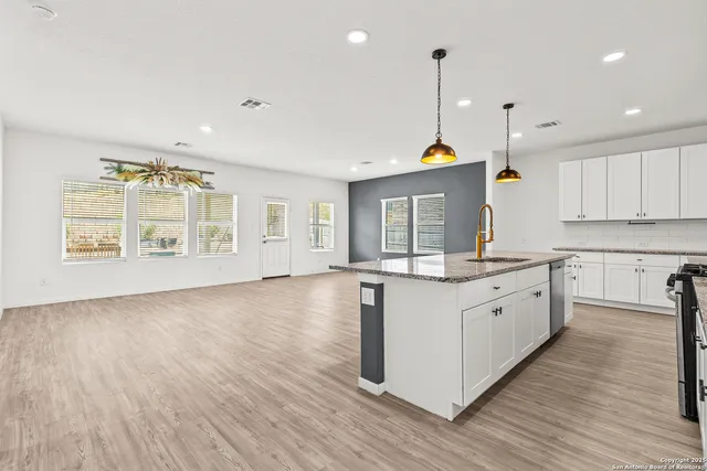 a kitchen with stainless steel appliances granite countertop a sink a stove a refrigerator and white cabinets with wooden floor