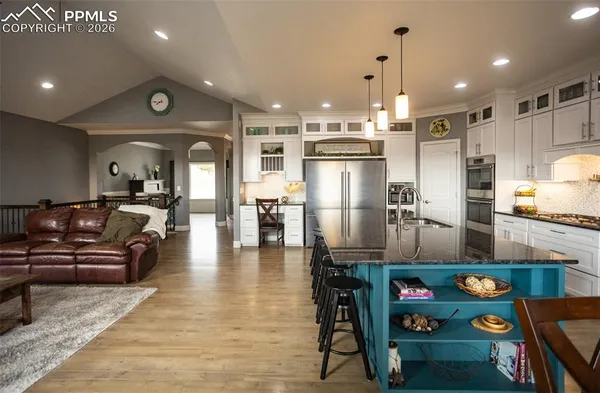 a kitchen with stainless steel appliances kitchen island granite countertop a refrigerator a stove a oven and a dining table with wooden floor