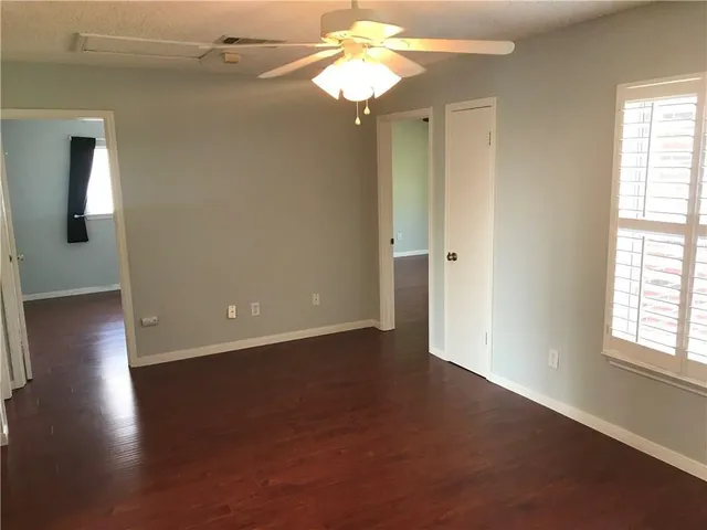 an empty room with wooden floor fan and windows