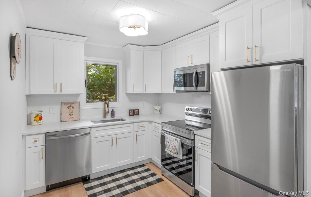 164 Maple Road Wading River, NY 11792 - Photo 10 of 19 Kitchen featuring appliances with stainless steel finishes, white cabinets, light wood-style flooring, crown molding, and light stone counters