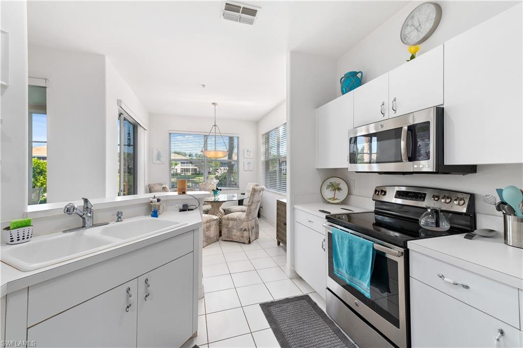 800 Carrick Bend Circle, Unit 103 Naples, FL 34110 - Photo 10 of 30 Kitchen featuring stainless steel range with electric cooktop, white cabinetry, light countertops, light tile patterned flooring, and hanging light fixtures