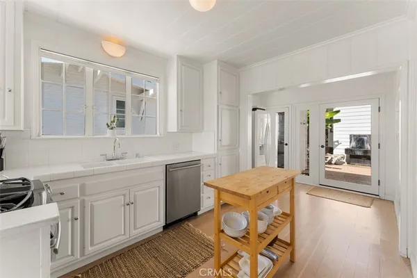 a large white kitchen with granite countertop a sink and dishwasher a stove with wooden floor