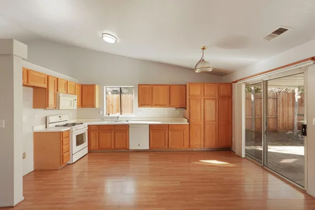 a large kitchen with granite countertop a stove a sink dishwasher and a refrigerator with wooden floor