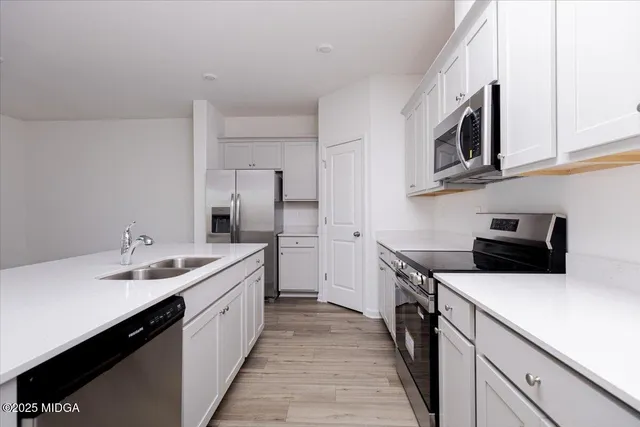 a kitchen with stainless steel appliances a sink stove oven a refrigerator with white cabinets and wooden floor