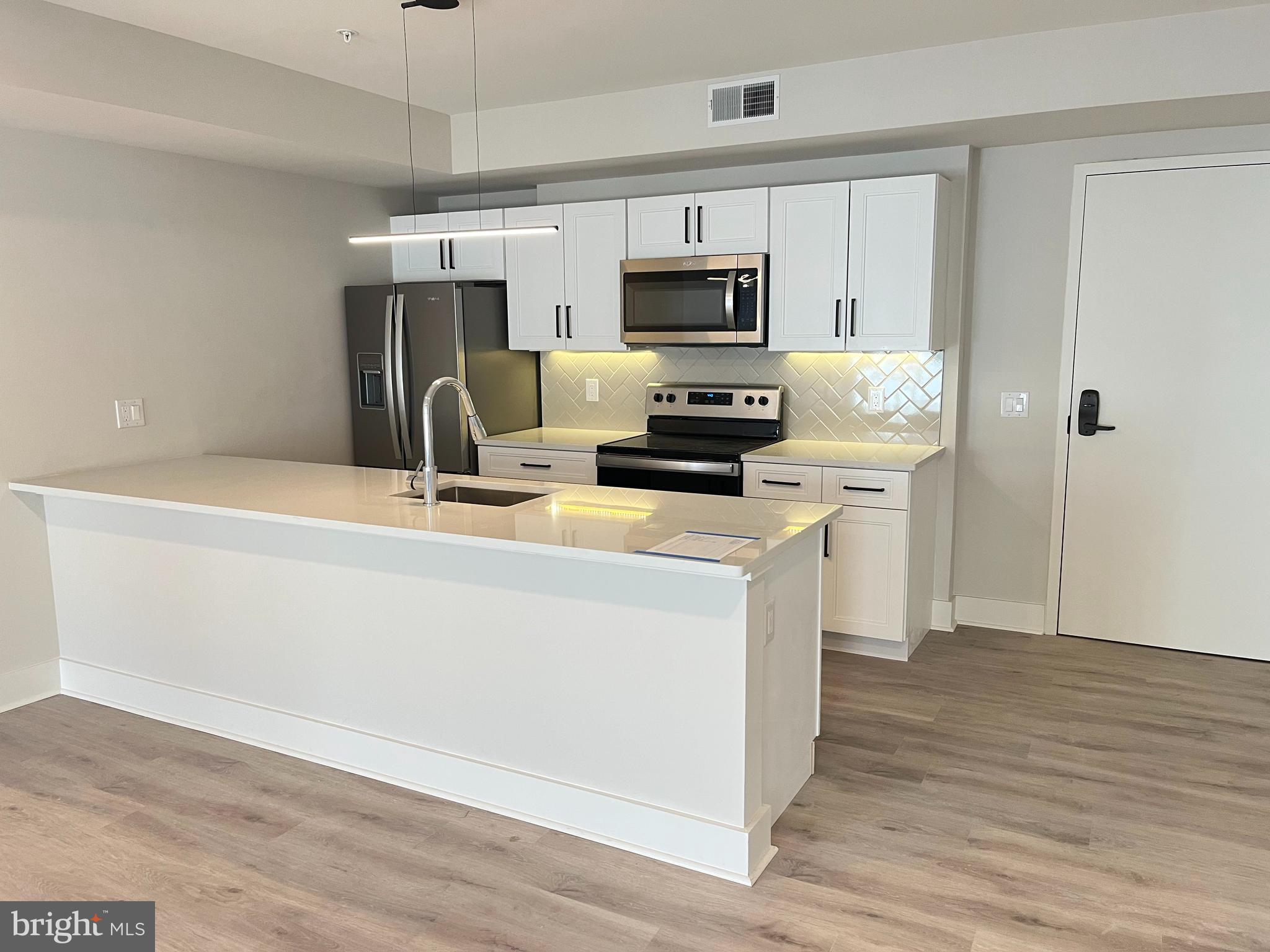 1805 North Howard Street, Unit 303 Philadelphia, PA 19122 - Photo 2 of 25 a kitchen with kitchen island white cabinets stainless steel appliances and wooden floor