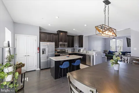 a kitchen with stainless steel appliances granite countertop a sink dishwasher a stove a refrigerator a dining table chairs and couches with wooden floor