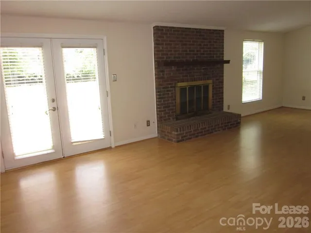 an empty room with wooden floor fireplace and windows