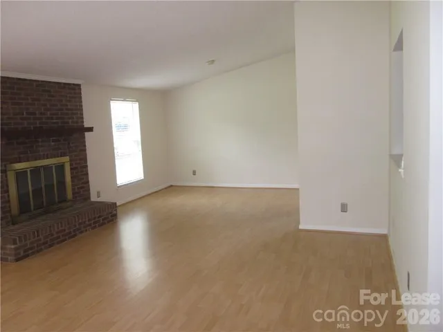 an empty room with wooden floor fireplace and windows