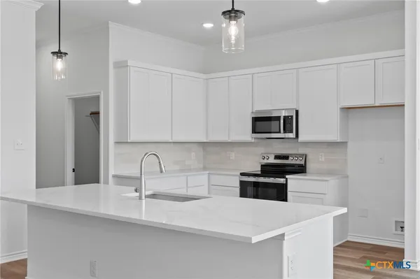 a kitchen with stainless steel appliances a sink a stove a microwave a sink a refrigerator and white cabinets