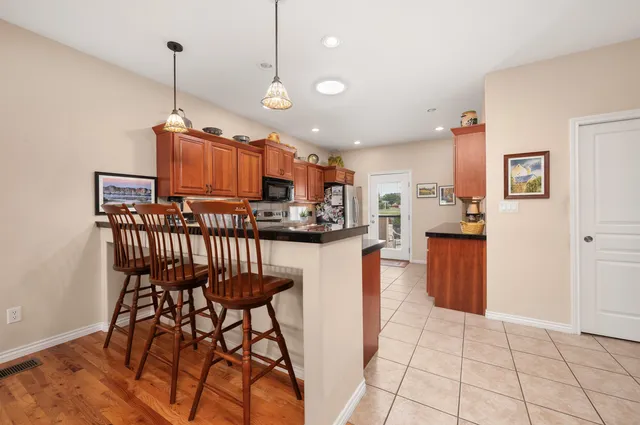 a open kitchen with stainless steel appliances granite countertop a stove top oven a sink a dining table and chairs with wooden floor