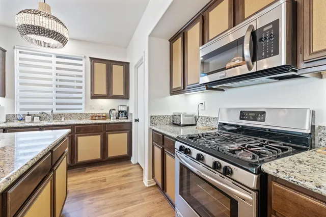 a kitchen with stainless steel appliances kitchen island granite countertop a stove a sink a dining table and chairs with wooden floor