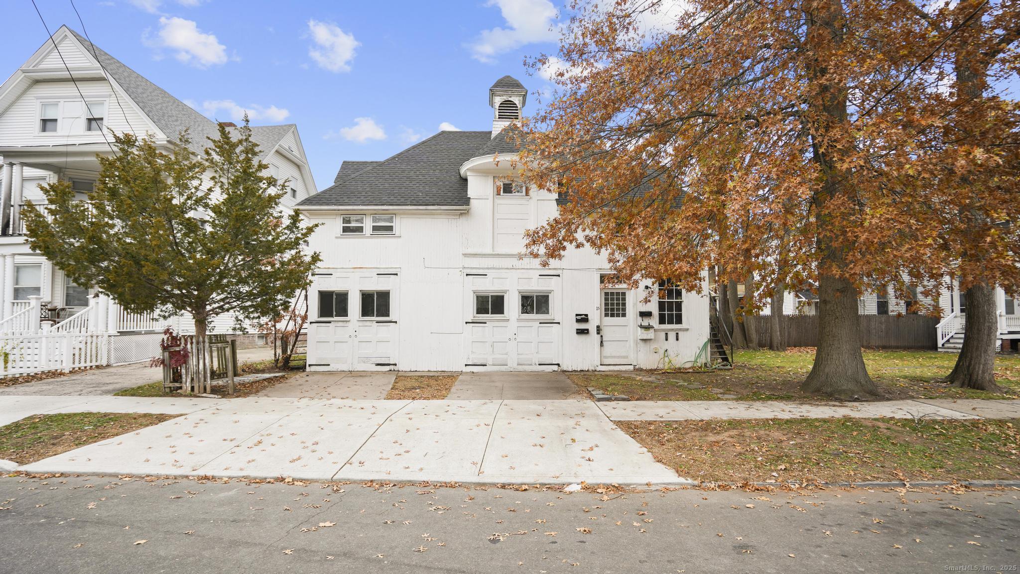 a view of a white house next to a road with large trees