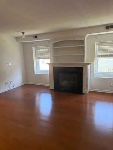 an empty room with wooden floor fireplace and windows
