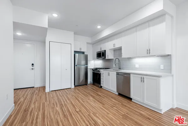 a kitchen with stainless steel appliances granite countertop a refrigerator a sink dishwasher a stove and white countertops with wooden floor