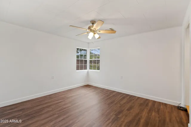 a view of an empty room with wooden floor and a ceiling fan
