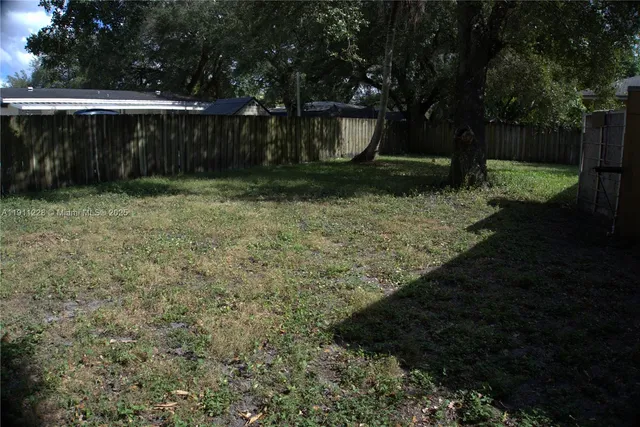 a view of a backyard with large trees and wooden fence