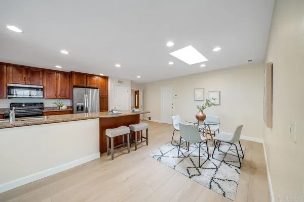 a kitchen with stainless steel appliances kitchen island granite countertop a refrigerator a stove a dining table and chairs with wooden floor