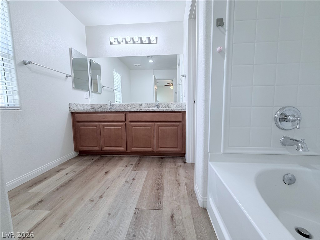 3610 Wireless Court Las Vegas, NV 89129 - Photo 7 of 15 A generous vanity with dual sinks, warm wood cabinetry, and sleek plank flooring elevate this primary bathroom.