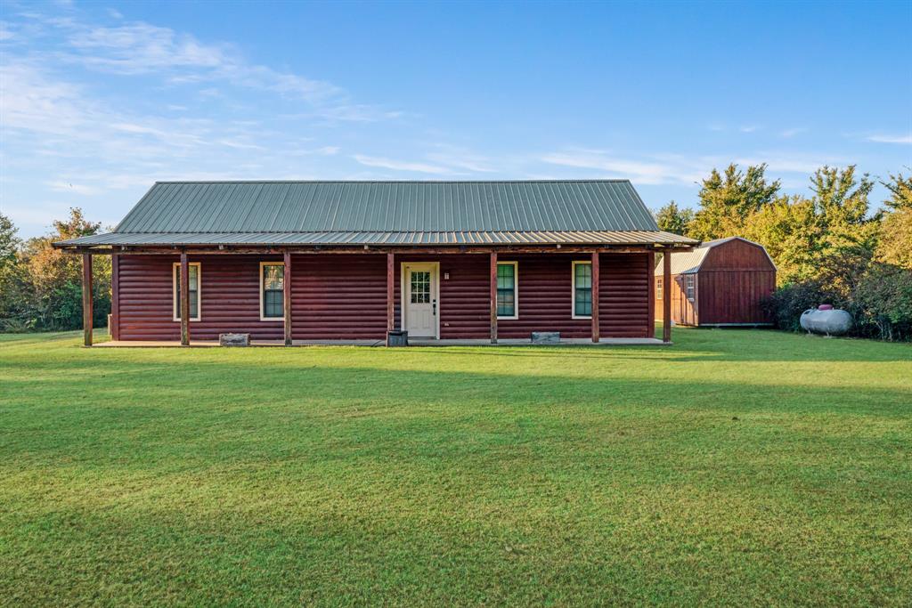 74 County Road Powderly, TX 75473 - Photo 1 of 1 View of front of property featuring log veneer siding, a metal roof, an outbuilding, and a front lawn
