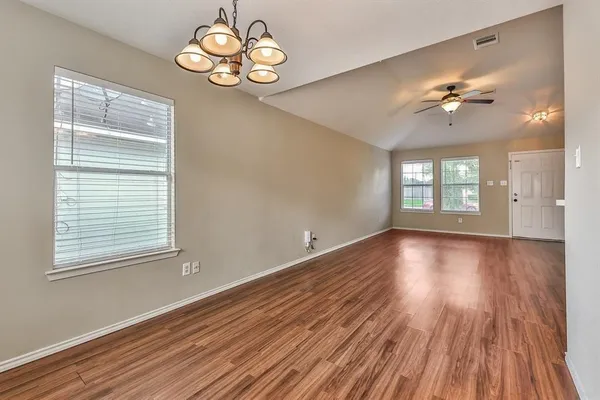 an empty room with wooden floor chandelier fan and windows