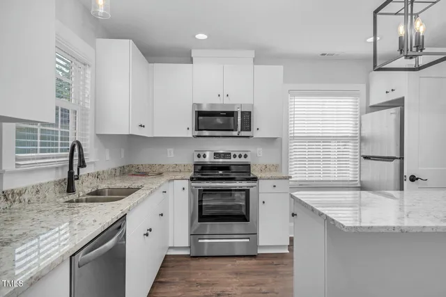 a kitchen with stainless steel appliances granite countertop a sink dishwasher a stove and a refrigerator with wooden floor