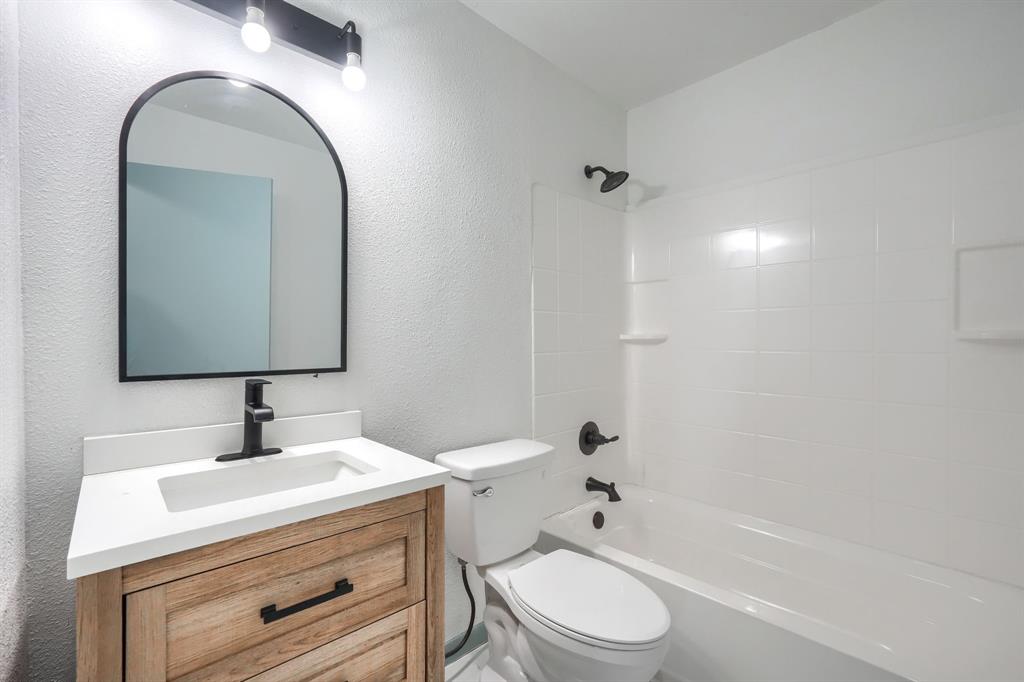 1802 Refinery Road Gainesville, TX 76240 - Photo 12 of 27 Bathroom featuring a wood-finish vanity with a white countertop and integrated sink, matte black faucet, and an arched mirror with a black frame