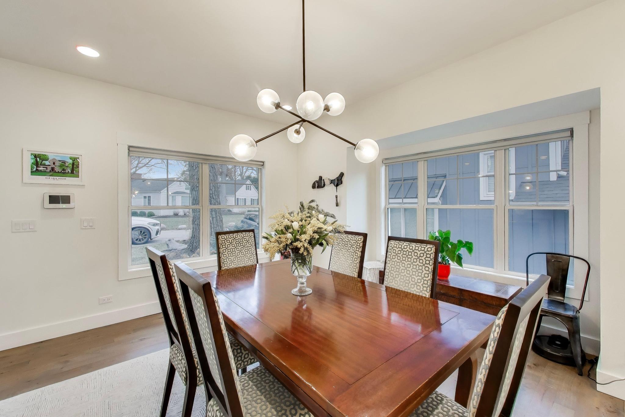 603 Agaming Road Fontana, WI 53125 - Photo 8 of 68 Sunlit dining room with contemporary lighting and large windows, offering an inviting setting for everyday meals or special occasions.