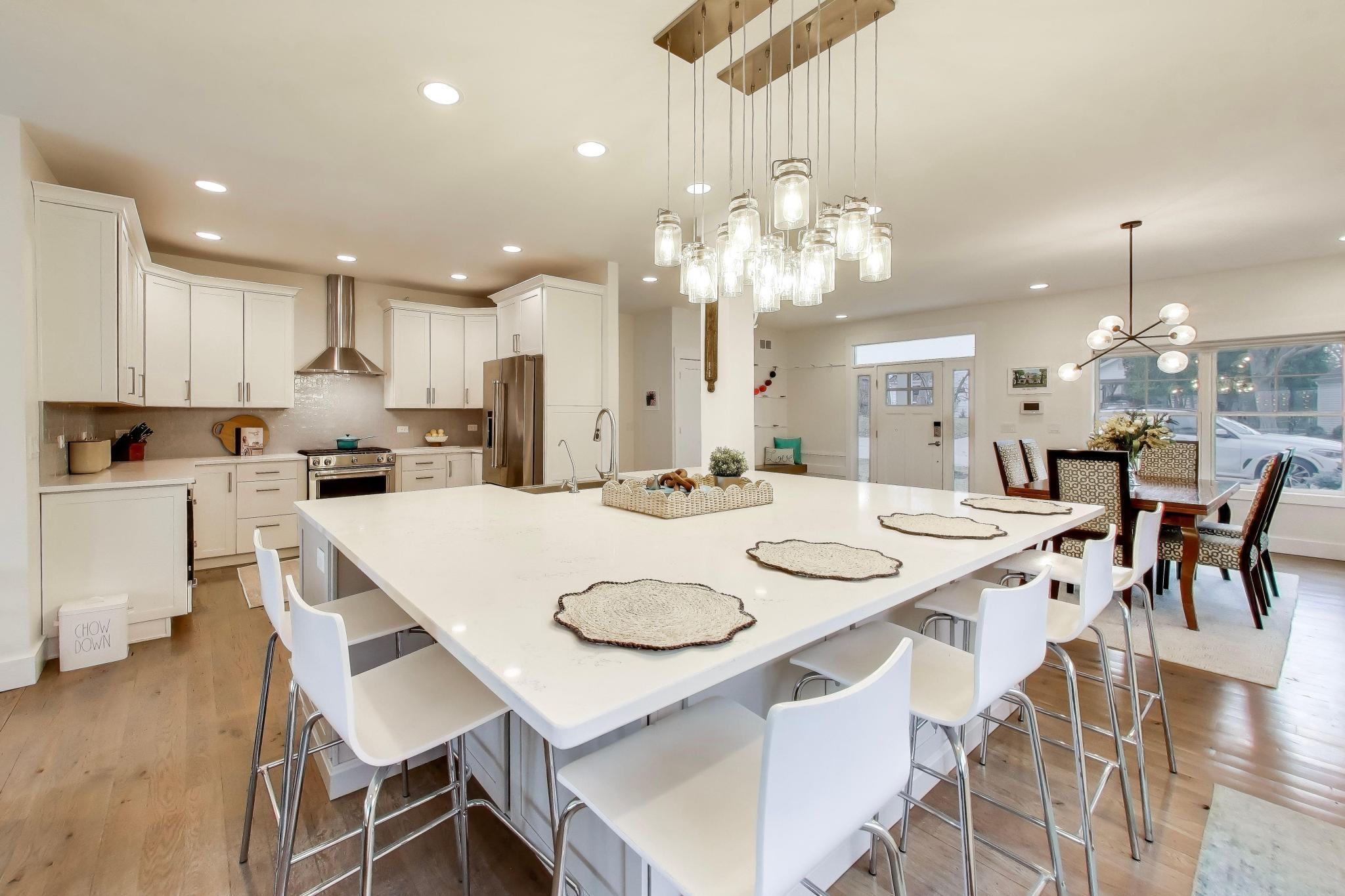 603 Agaming Road Fontana, WI 53125 - Photo 11 of 68 Bright, open kitchen featuring a generous quartz island with seating, custom cabinetry, stainless steel appliances, and designer pendant lighting. Ideal for entertaining and everyday living.