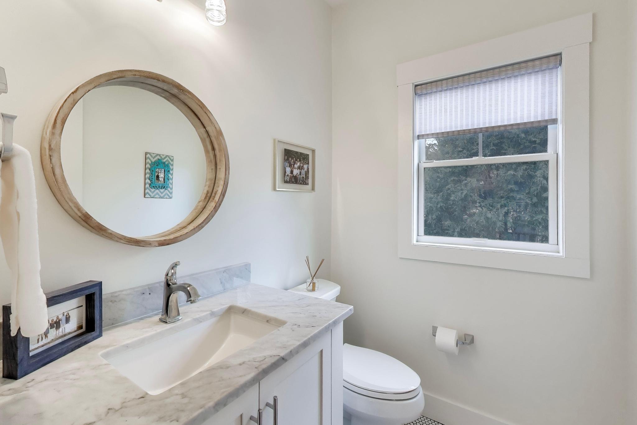 603 Agaming Road Fontana, WI 53125 - Photo 23 of 68 Stylish main-level powder room with marble vanity top, round accent mirror, and window providing natural light.
