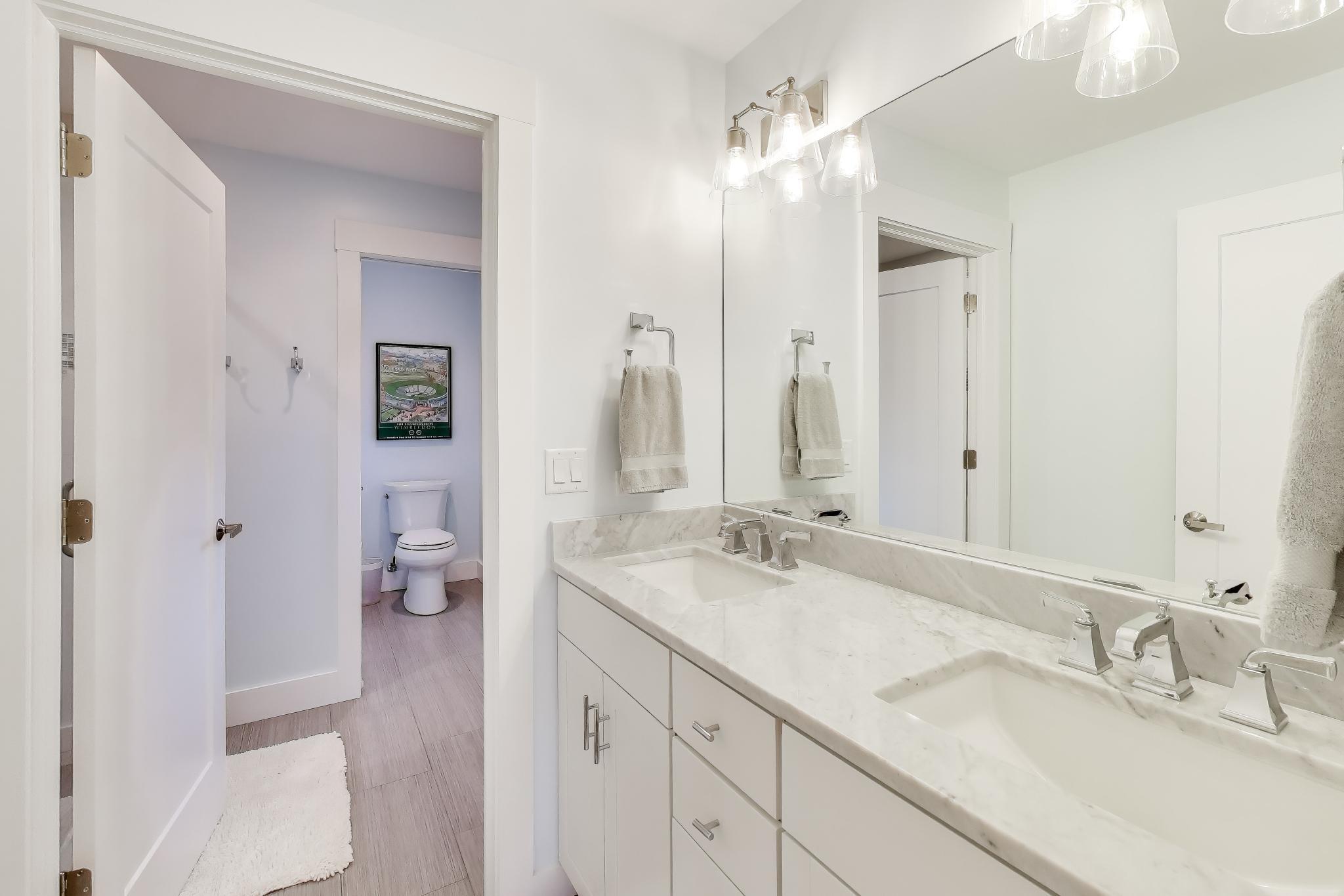 603 Agaming Road Fontana, WI 53125 - Photo 36 of 68 Bright bathroom with dual sinks, marble countertops, modern fixtures, and a large mirror for added functionality.