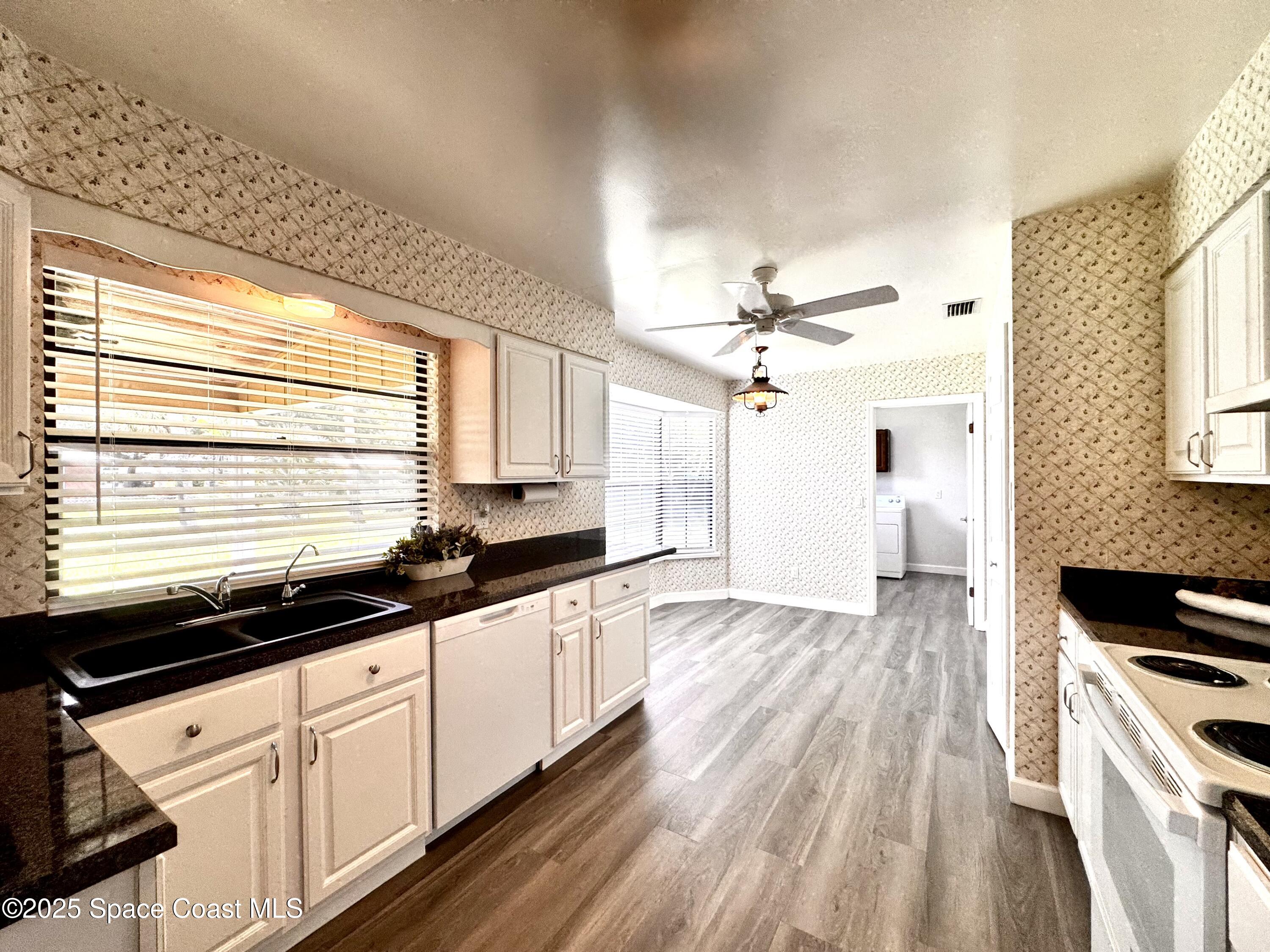 658 Ervin Street Sebastian, FL 32958 - Photo 11 of 36 a kitchen with granite countertop a stove a sink and white cabinets with wooden floor
