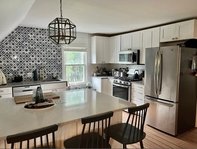 a kitchen with stainless steel appliances granite countertop a dining table chairs refrigerator and sink