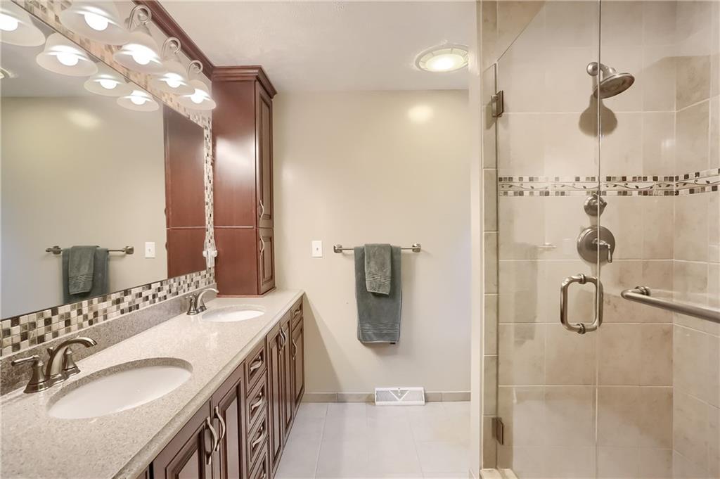 233 Foxglove Road Baden, PA 15005 - Photo 17 of 25 Relax in the updated master bath with a tile shower featuring a bench seat and glass door. Dual sink quartz topped vanity and custom cabinetry with built in outlets are complimented with a custom tile back splash.