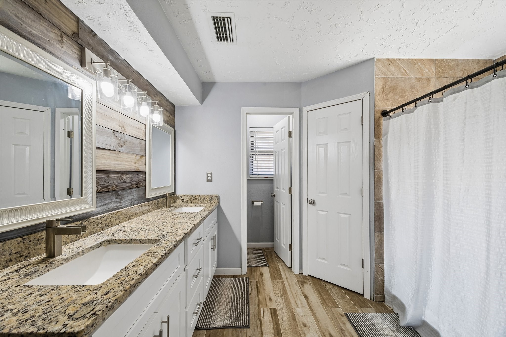 23115 Stepinwolf Lane Spring, TX 77373 - Photo 16 of 18 Elegant bathroom featuring a spacious double vanity with granite countertops, rustic wood accents, and a tiled shower area with a classic curtain.