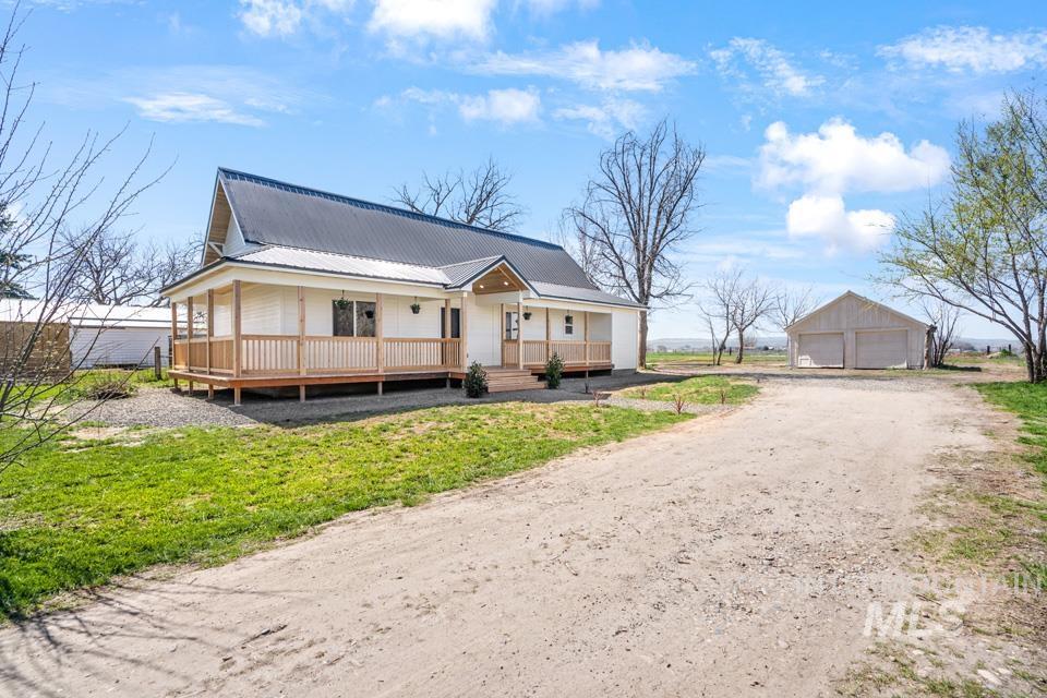 View of front of home featuring a porch, an outbuilding, a garage, a metal roof, and a front lawn