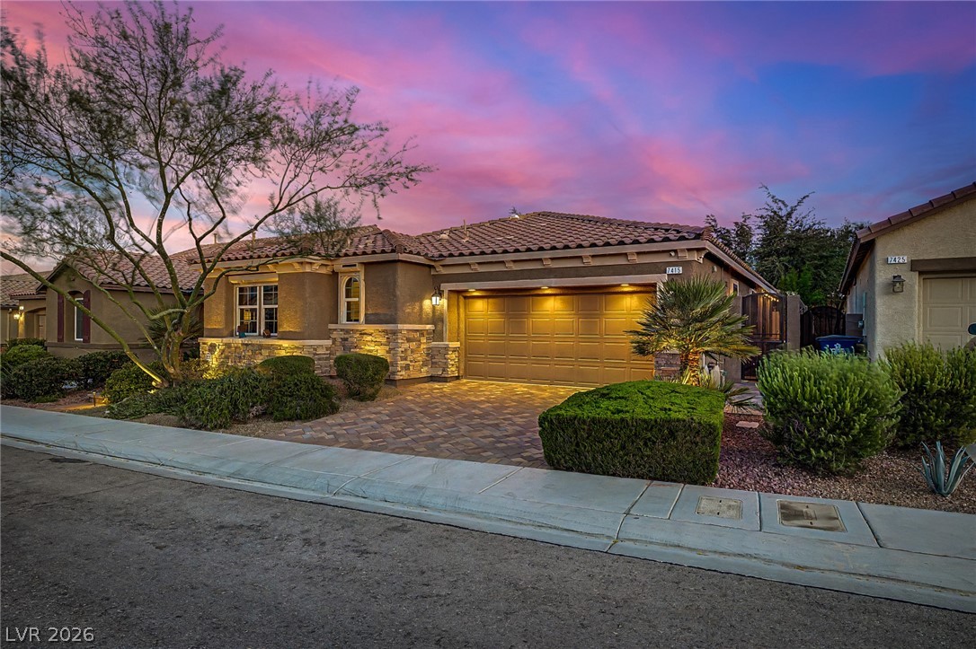 7415 Campbell Ranch Avenue Las Vegas, NV 89179 - Photo 6 of 52 A well-maintained facade features a paver driveway, stone accents, and inviting landscape lighting at dusk.