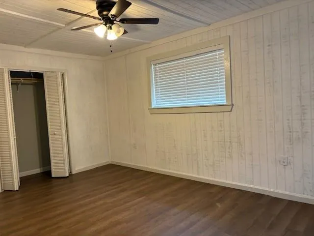 an empty room with wooden floor chandelier fan and windows