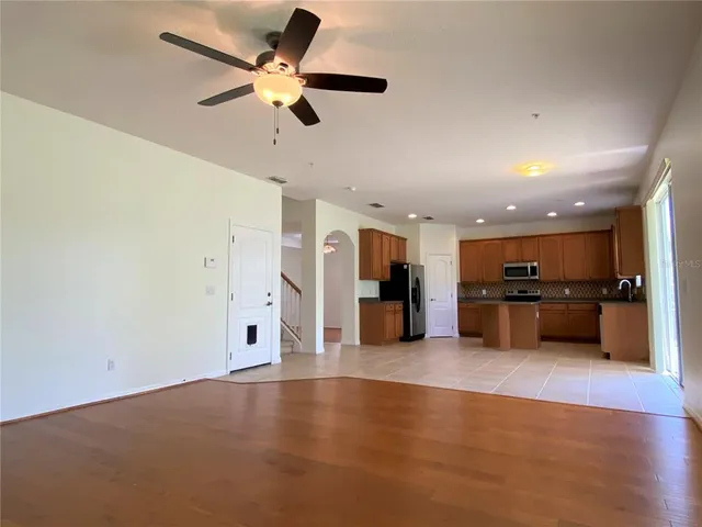a view of an empty room with a ceiling fan and kitchen