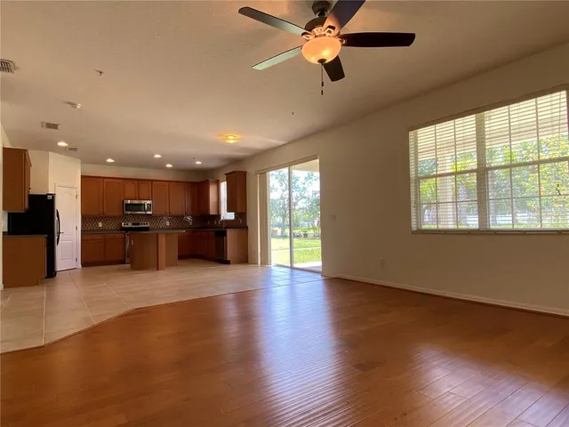 a view of an empty room with wooden floor and a kitchen