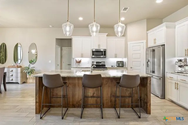 a kitchen with stainless steel appliances kitchen island granite countertop a dining table chairs and a refrigerator