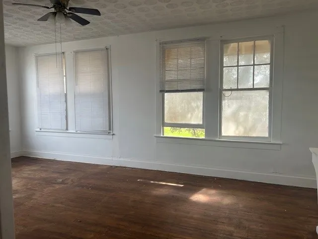 an empty room with wooden floor chandelier fan and windows