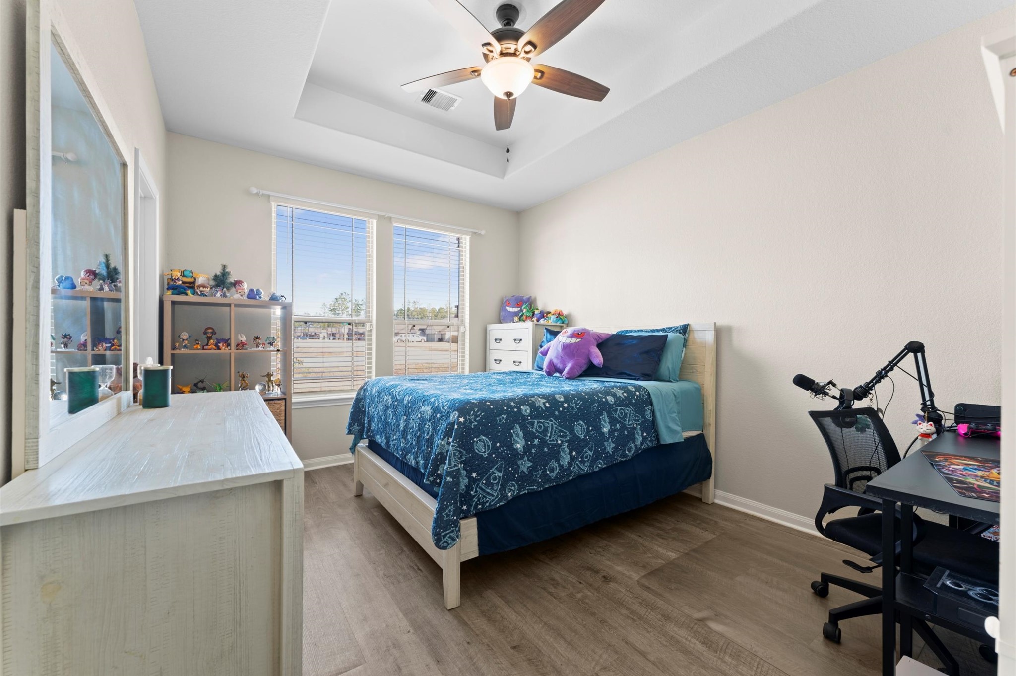 9729 Hidalgo Street Conroe, TX 77303 - Photo 26 of 38 This cozy bedroom features a ceiling fan, tray ceiling, natural light from large windows, and wood-look vinyl flooring. The room is well-lit and inviting, perfect for a child or guest room.
