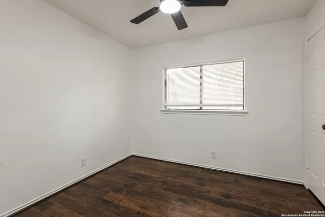 an empty room with wooden floor chandelier fan and windows