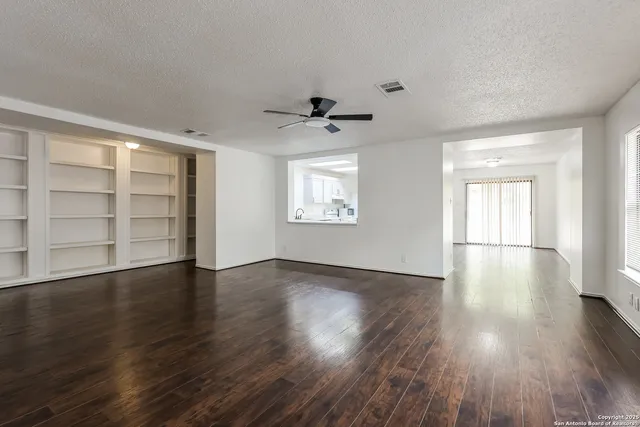an empty room with wooden floor chandelier and windows